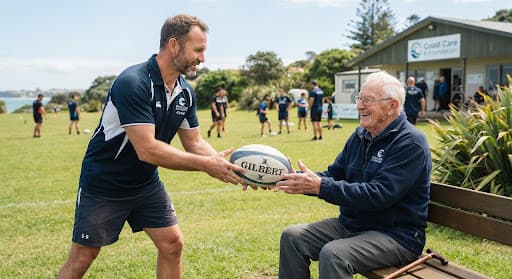 A Coast Care Rugby coach handing a rugby ball to a seated resident outdoors